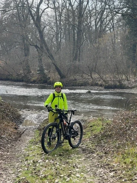 un uomo in una giacca gialla che tiene una bicicletta in riva a un fiume