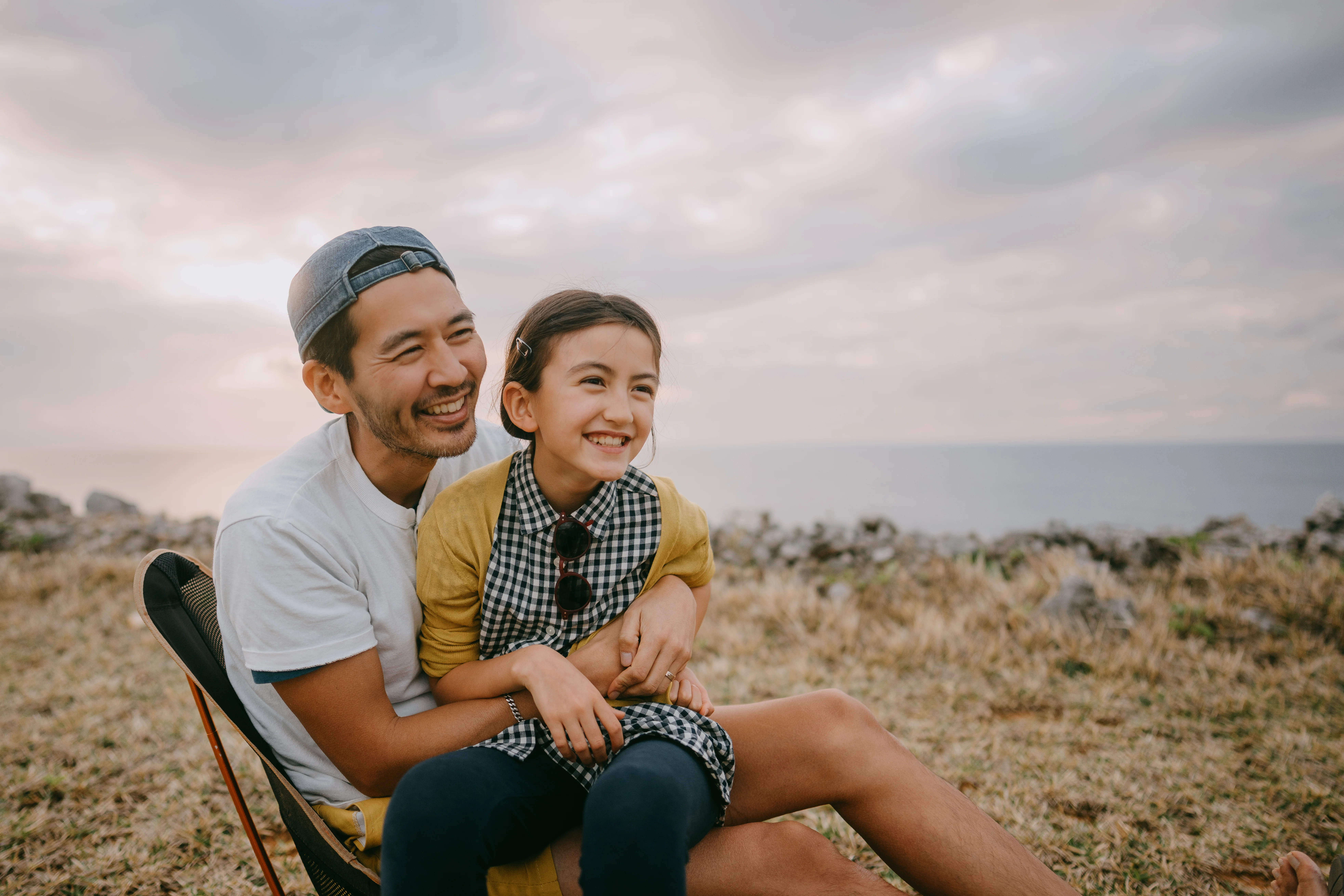 A man and his daughter laughing by the sea. 